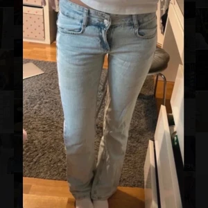 Ljusblå bootcut  jeans Pull&Bear - Säljer ett par ljusblå jeans från Pull&Bear i storlek 34. Jeansen har klassisk femficksmodell, raka ben och normal passform. Tillverkade i bomull med snygg tvättad look och dubbla silverknappar i midjan. Perfekta för en chill och trendig stil.