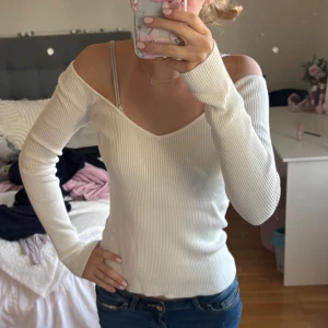 Ribbad thight tröja - Supersnygg vit ribbad tröja med offshoulder och v-ringning. Långärmad och figurnära passform som sitter riktigt snyggt. Perfekt till jeans eller kjol för en trendig look.