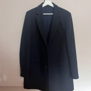 Mörkblå rock Jasper Conran 40R - Stilren mörkblå rock från Jasper Conran i klassisk modell med två knappar framtill och fickor med lock. Perfekt för dig som gillar en tidlös look. Fodrad insida och snygg passform. Storlek 40R.