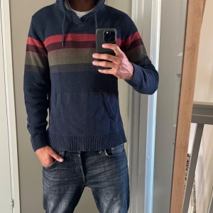 hoodie från Commerce, marinblå - Snygg stickad hoodie från Commerce i marinblått med breda ränder i rött, vinrött och olivgrönt över bröstet. Tröjan har huva med snörning, känguruficka och långa ärmar. Bra skick storlek S, passar mig som är 180cm och 75kg, tveka inte att skriva vid funderingar 💯