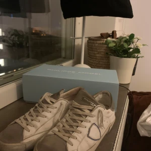 Philippe Model vita sneakers strl 40 - Snygga vita Philippe Model sneakers i klassisk low-top modell med grå detaljer och logga på sidan. Skorna har snörning, rund tå och en robust sula med Philippe Model-tryck undertill. Perfekta för dig som gillar stilrena och trendiga sneakers. Dustbag och kvitto kommer med