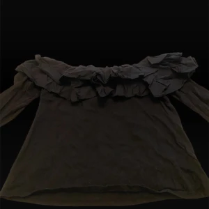 Svart offshoulder blus med volang - Supersnygg svart offshoulder blus med stora volanger längs halsringningen. Tunt och lätt material som ger en luftig känsla. Långa ärmar och en feminin, romantisk vibe. Perfekt för dig som vill sticka ut lite extra.