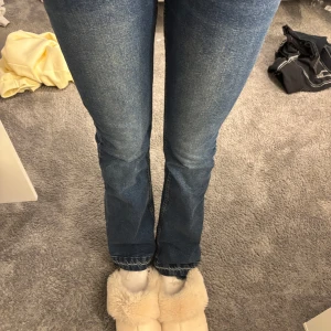 Blå bootcut jeans med dragkedja bak - Säljer ett par blå bootcut jeans som är lågmidjade, uppsprätta där nere då de var förkortade men passar perfekt nu! (167) (de har slitit slita på högra sidan där man drar upp byxorna men inte gått av helt!!!)