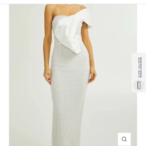 Vit långklänning med rosett - Supersnygg vit långklänning med axelbandslös design och stor rosettdetalj framtill och pärlbroderier över hela klänningen. Säljer för 1500 men pris kan diskuteras! 