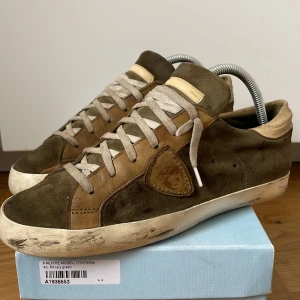Philippe Model Paris skor - Sneakers från Philippe Model i militärgrön med beige detaljer. Klassisk låg modell med snörning och vit sula. Snyggt logomärke på sidan. Perfekta för dig som gillar finare utklädning. Sänker priset eftersom sulan lossnat lite som man ser på bilden!