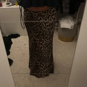 Långkjol - Säljer en lång kjol med leopardmönster i bruna och svarta toner. Kjolen har en figurnära passform och faller snyggt längs benen. Perfekt för dig som vill sticka ut med en trendig och djurisk look.