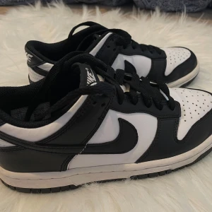 Nike Dunk Low svart/vit sneakers - Aldrig lägga.Snygga Nike Dunk Low sneakers i svart och vitt med klassisk design. Skorna har svart läder på overlays och vit bas, svart swoosh och snörning. Perfekta för dig som gillar streetstyle och vill ha en ikonisk sneaker i garderoben.
