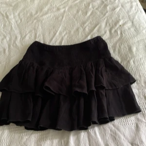 Svart volangkjol från SHEIN XXS - Supersöt svart kortkjol från SHEIN i storlek XXS. Kjolen har flera lager volanger och en smockad midja som ger en snygg passform. Perfekt för dig som gillar en lekfull och trendig stil. Lätt och luftig, passar till många olika outfits.