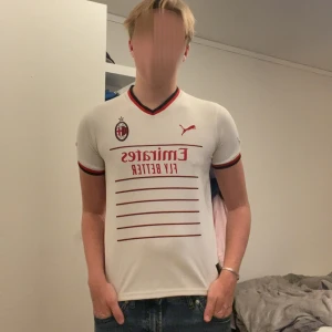 AC Milan vit bortatröja Puma M - AC Milan bortatröja från Puma i vitt med röda och svarta detaljer. Broderat klubbmärke och Puma-logga på bröstet, röd sponsorlogga och tunna röda linjer framtill. V-ringad krage med röd och svart kant. Så Tillverkad i lätt, ventilerande material. Passar storlek xxs