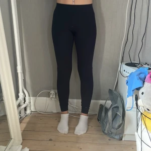 Svarta leggings från Ronhill - Svarta leggings från Ronhill i stretchigt syntetmaterial. De har hög midja och tight passform, perfekta för träning eller chill. Snygga detaljer i tyget på sidorna och diskret logga på höften. Superbekväma och följsamma.