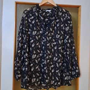 Svart blommig blus från Ellos - Snygg svart blus från Ellos med beige blommigt mönster. Blusen är i ett tunt, transparent material och har v-ringning samt långa ärmar med resår vid ärmslut. Perfekt för dig som gillar en luftig och stilren look. Den är I jättefint skick:)