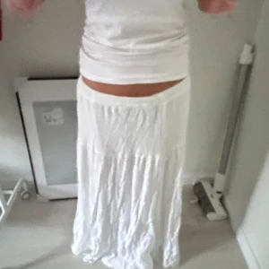 Vit långkjol i bomull - Säljer en flowy vit långkjol med lätt rynkad struktur och bred midja. Kjolen är i mjuk bomull och har en luftig känsla som passar perfekt till varma dagar. Enkel och stilren design som är lätt att matcha med olika toppar.