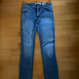 Levi's 511 ljusblå jeans 14A/164 - Säljer ett par klassiska Levi's 511 jeans i ljusblå tvätt. Modellen är slim och har raka ben med normal midja. Jeansen är tillverkade i bomull och har fem fickor samt dragkedja och knapp framtill. Perfekta för en clean och avslappnad look.