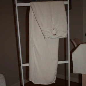 Beige linne långkjol med ringdetalj - Snygg beige långkjol i bomull med en unik ringdetalj i midjan. Kjolen har en rak passform och är enkel men ändå trendig, perfekt för dig som gillar minimalistisk stil. Materialet känns luftigt och passar bra till varmare dagar.