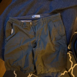 Gröna shorts från lager 157, storlek S - Snygga gröna shorts från 157 i storlek small. Klassisk modell med fickor på sidorna och knapp- samt dragkedjestängning. Perfekta för varma dagar och enkel att matcha med t-shirt eller linne.