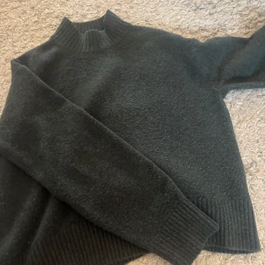 Mörkgrön stickad tröja från Uniqlo - Säljer en stilren mörkgrön stickad tröja från Uniqlo. Tröjan har en kort krage och långa ärmar med ribbade muddar. Perfekt för kyliga dagar. Hör av dig vid intresse!