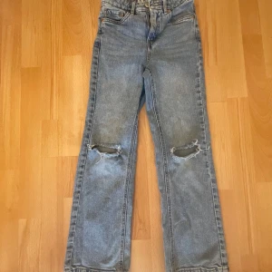 Blå jeans med slitna knän - Säljer ett par coola blå jeans med slitna detaljer på knäna. De har en klassisk femficksdesign och en bekväm passform. Perfekta för en avslappnad stil.