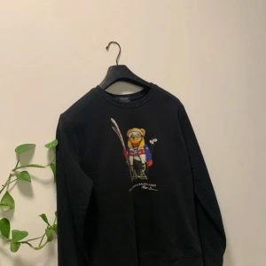 Svart tröja med Polo Bear från Ralph Lauren - Säljer en svart tröja ( strl 170 ) från Ralph Lauren med en ikonisk Polo Bear-illustration på framsidan 🤩. Björnen är klädd i skidutrustning med färgglada detaljer. Tröjan är också tillverkad i en mjuk bomullsblandning. Nypris cirka 1400 kr. 