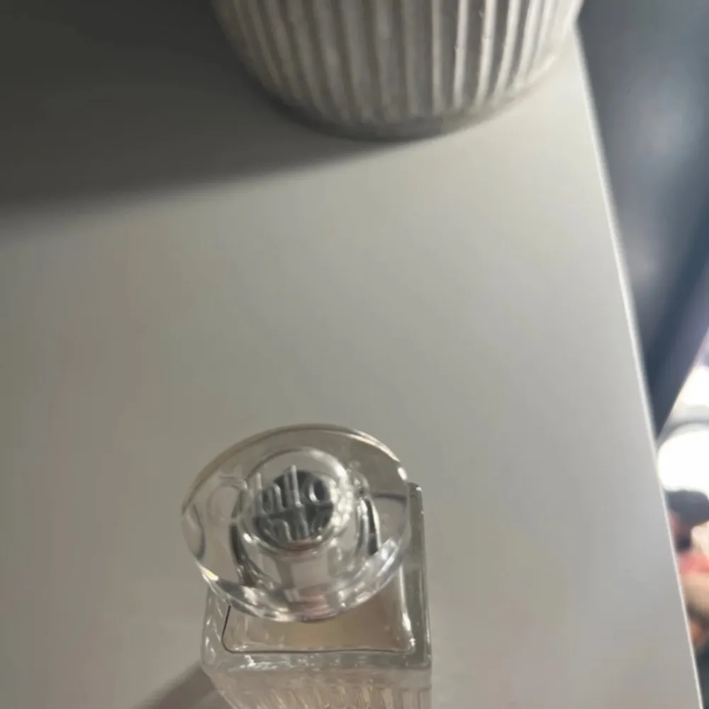 Snygg parfymflaska med en elegant räfflad design och genomskinligt glas. Flaskan har en fyrkantig form och ett stilrent lock i silverfärg. Perfekt för den som vill ha en tidlös och klassisk look på sitt sminkbord.. Perfume.