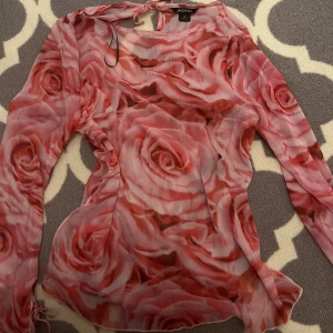 Rosa blommig topp från Monki - Säljer en snygg rosa blommig topp från Monki. Toppen har ett vackert ros-mönster och långa ärmar med knytning vid ärmsluten. Perfekt för att ge en romantisk touch till din outfit. 🌹