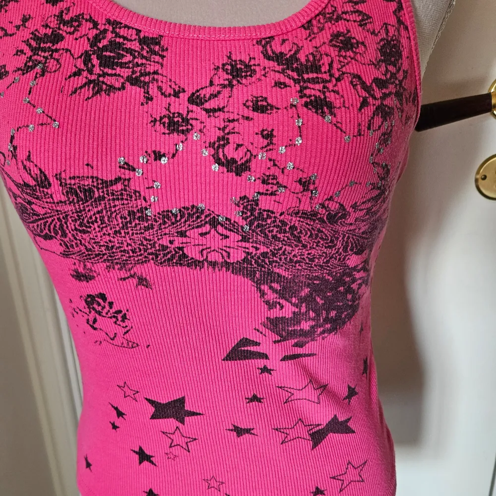 Rosa ribbat linne med tryck av blommor och stjärnor framtill. Racerback-design. Tyvärr är lappen bortklippt. Yläosat.