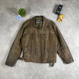 Vintage 90s Faded Distressed Boxy Cropped Oversized Brown Leather Jacket - Skinnjacka i äkta läder med en vackert sliten och patinerad brun nyans som ger en tidlös vintagekänsla. Jackan har en boxig och oversized passform med en croppad längd som ger en modern och edgy look. Längd 68 cm, bredd 59 cm och ärmlängd 62 cm, vilket gör den perfekt för en avslappnad streetwear-stil eller som ett statement-plagg i din garderob. Naturligt slitage ger jackan extra karaktär och gör den helt unik. Finns ett minimalt hål vid fickan, men syns knappt vid användning.