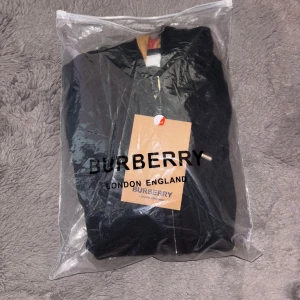 Svart hoodie från Burberry.  - Säljer en helt ny oanvänd stilren svart hoodie från Burberry med dragkedja och klassiskt rutigt mönster i huvan. Perfekt för en casual look med en touch av lyx. 🖤Säljer denna eftersom att den var för liten för mig😴