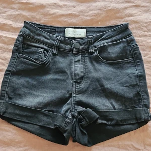 Svarta jeansshorts från Pieces - Snygga svarta jeansshorts från Pieces med hög midja och uppvikta ben. Perfekta för en avslappnad stil. De har klassiska fem fickor och knappgylf.