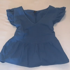 Blå blus från Shein - Säljer en söt blå blus från Shein med v-ringning och korta puffärmar. Blusen har en lätt volangdetalj vid midjan.