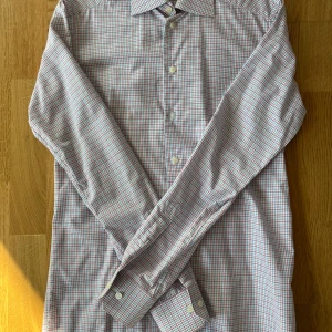 Rutig skjorta från Eton - Säljer en stilren rutig skjorta från Eton, rutnätet är rött och blått och resten av skjortan är vit. Skjortan har en slim passform och är långärmad med knappar framtill. Perfekt för en snygg och klassisk look.