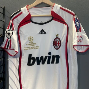 Vit AC Milan fotbollströja med Kaka 22 - Säljer en vit AC Milan fotbollströja från Adidas med Kaka's namn och nummer 22 på ryggen. Tröjan har röda och svarta detaljer samt Champions League-märken på ärmarna. Perfekt för samlare eller fans av Kaka och AC Milan en replika i storlek S. Helt ny med tagg