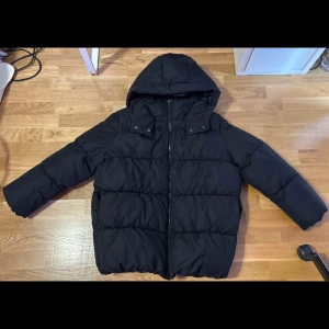 Svart pufferjacka från Vero Moda - Säljer en svart pufferjacka med luva. Jackan har en dragkedja framtill och långa ärmar. Perfekt för kyligare dagar. Dock är den helt ny/ej använd.