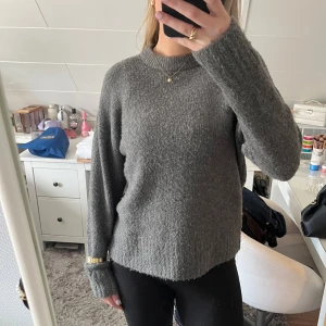Grå stickad tröja - Säljer en mysig grå stickad tröja med rund hals och långa ärmar. Perfekt för kyligare dagar och enkel att matcha med olika outfits. Tröjan har en avslappnad passform i använt skick som ni ser på bilderna (noppor)