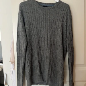 Grå stickad tröja från Jack & Jones - Säljer en stilren grå stickad tröja från Jack & Jones. Tröjan har ett klassiskt kabelstickat mönster och långa ärmar. Perfekt för kyligare dagar.