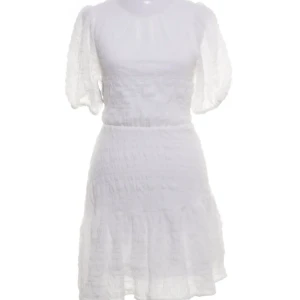 Vit klänning med puffärmar - Vit klänning med puffiga kortärmar och knytning i ryggen. Den har en luftig och texturerad design med volangdetaljer vid fållen. Perfekt till studenten eller för en somrig look! Aldrig använd men bortdragen prislapp. Pris kan diskuteras.
