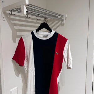 Flerfärgad t-shirt från Lacoste - Snygg t-shirt från Lacoste i en cool färgblockdesign med rött, vitt och blått. Den har en klassisk krokodil-logga på bröstet och korta ärmar. Perfekt för en avslappnad stil.