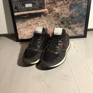 Svarta sneakers från Philippe Model - Vill du ha skor som sticker ut utan att ta över? 👀 De här Philippe Model-sneakersen mixar lyxig design med avslappnad streetstyle. ✨ Mocka, mesh och läder ger både komfort och stil, medan röda detaljer och slitstark sula sätter pricken över i:et. 👟 OBS! Priset är ej hugget i sten! OBS! Dustbag med följer fråga vid intresse av bild!