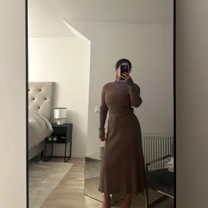 Brun ribbad klänning - Snygg brun ribbad klänning med lång ärm och figurnära passform. Perfekt för en stilren look. Klänningen har en elegant midilängd och är tillverkad i ett mjukt material.