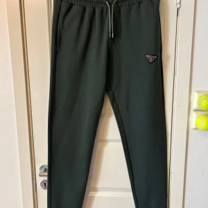 Gröna mjukisbyxor från Prada - Snygga gröna mjukisbyxor från Prada med elastisk midja och dragsko. Byxorna har en bakficka och en diskret logotyp på framsidan. Perfekta för en avslappnad stil med en touch av lyx. Dom passar även dig som har M