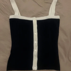 Mörkblå och vit kashmir topp från Cloeys - Snygg mörkblå linnetopp i kashmir med vita detaljer från Cloeys. Toppen har knappar framtill och breda axelband. Perfekt för en stilren look.. helt ny