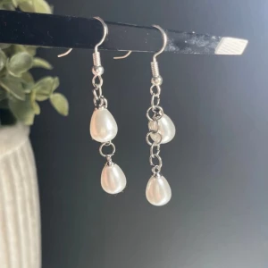 Örhängen med vita pärlor - Eleganta örhängen med vita pärlor i droppform. De hänger i en silverfärgad kedja och har en enkel krok för att fästa i örat. Perfekta för att ge en klassisk touch till din stil.