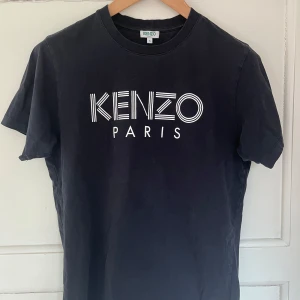 Svart t-shirt från Kenzo - Snygg svart t-shirt från Kenzo med deras ikoniska logga i vitt på bröstet. Perfekt för en stilren och modern look. 