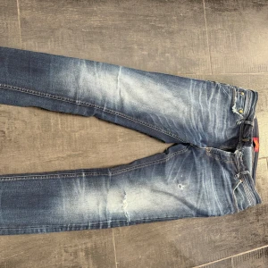 Jack & Jones jeans - Snygga blå skinny jeans med en sliten look och ljusa tvättade detaljer. Perfekta för en trendig stil. De har klassiska fem fickor och knappgylf.