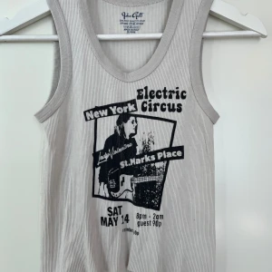 Grå ribbad linnetopp från Brandi Mellville - Säljer en cool grå ribbad linnetopp från Brandi Mellville med ett tryck av en konsertposter för 'Electric Circus' i New York. Perfekt för en avslappnad stil med en vintagekänsla. Tillverkad i Italien.