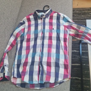 Rutig skjorta från Ralph Lauren - Säljer en snygg rutig skjorta från Ralph Lauren i färgerna blå, röd och vit. Skjortan har en klassisk krage och knappar framtill. Den är i slim fit och har långa ärmar. Perfekt för en stilren look!