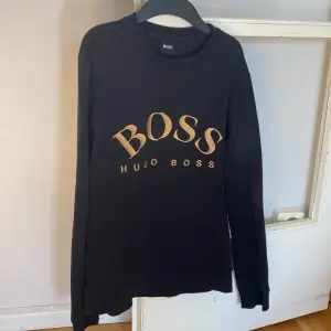 Säljer en stilren svart tröja från Hugo Boss med deras ikoniska logga i guld på bröstet. Tröjan har långa ärmar och en klassisk rund halsringning. Perfekt för en avslappnad men ändå elegant look👍🏻