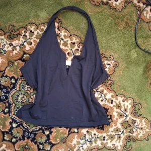 Svart halterneck topp - Snygg svart halterneck topp med djup v-ringning. Perfekt för en stilren look. Toppen har en enkel design som gör den lätt att matcha med olika outfits.