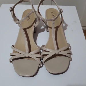 Beige sandaler med klack - Snygga beige sandaler från Alley med en elegant klack och öppen tå. De har smala remmar som korsar över foten och en justerbar rem runt ankeln för perfekt passform. Perfekta för sommarens alla tillfällen!