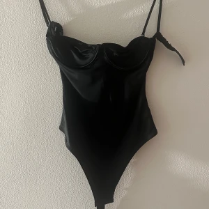Svart body från HM - Skit snygg svart body från HM. Den sitter riktigt tight och ser glansig ut på. Aldrig använda och säljer för att den är för liten för mig. Skulle säga att den är i xs/s. Och  i 75b. Öppen rygg