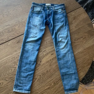 Blå jeans från Replay - Snygga blå jeans från Replay, modell Anbass. Dessa jeans har en slim fit och är tillverkade i ett klassiskt denimtyg. De har en midwaist och en stilren design med fem fickor och knappgylf. Ny pris 1700. Använd 4 gånger så nästan helt nya. Storlek 28X32.